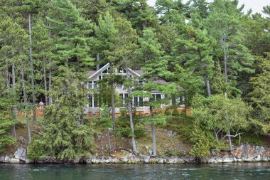 Gündüz vakti gölün kıyısındaki kayalık bir bölgede ıssız bir kulübede ve etrafı ağaçlarla çevrili. Gayrimenkul kavramı. Binlerce Adalar. Ontario, Kanada.