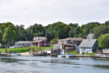 Gündüz vakti gölün kıyısındaki çimenli bir alanda ağaçlarla çevrili bir sürü farklı bina var. Gayrimenkul kavramı. Binlerce Adalar. Ontario, Kanada.
