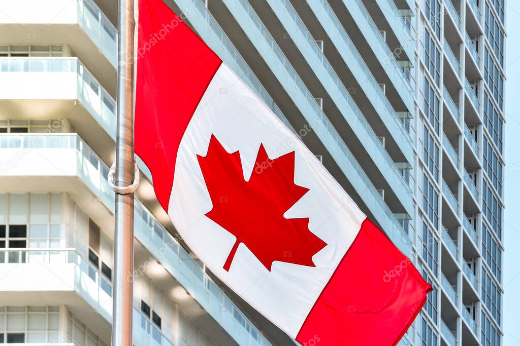 Canadian flag in daylight on a metal and glass office building background. Toronto, Ontario, Canada