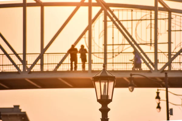 Unrecognizable couple contemplating the views on a bridge against the sunset. Streetlight in the foreground.