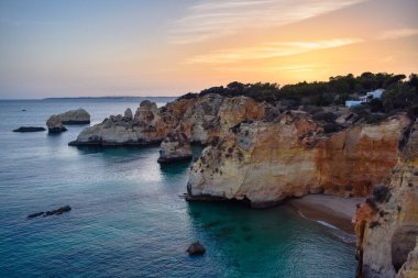 Kayalıkların tepesinde, gün batımında denize bakan küçük bir yazlık. Algarve, Portekiz