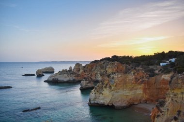Kayalıkların tepesinde, gün batımında denize bakan küçük bir yazlık. Algarve, Portekiz