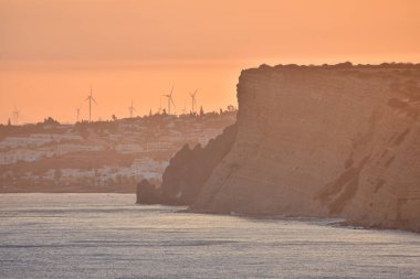 Sahildeki uçurumlarda, turistik dairelerde ve rüzgar değirmenlerinde güzel bir gün batımı. Turizm ve seyahat kavramı. Algarve, Portekiz