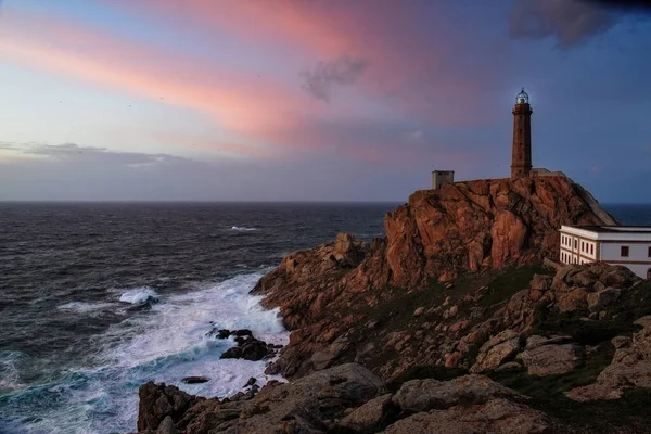 Lighthouse at Cabo Vilan on the Galician coast in a colourful sunset and with the sea in a rage. The oldest electric lighthouse in Spain. Galicia, Spain.