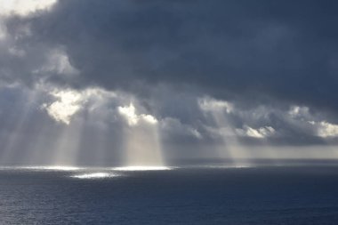 Bulutların üzerinden geçen ve denizi spot ışıkları gibi aydınlatan ışık huzmeleri. Doğa ve deniz kavramı. Galiçya, İspanya