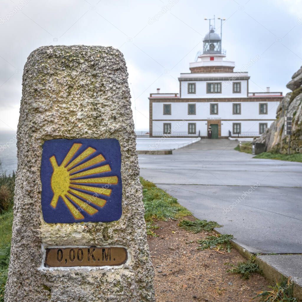 Sign of the Camino de Santiago and Finisterre Lighthouse in the background. In the light of day, in a sky with clouds. Galicia, Spain. Galicia, Spain