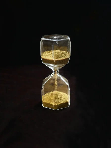 Siyah zemin üzerinde altın kum olan kum saati.