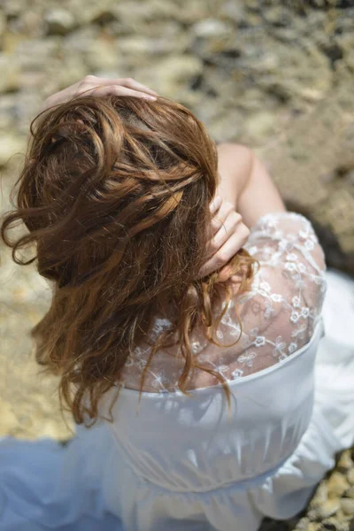 Beyaz elbiseli genç kadın dağınık saçlarını tutuyor. 