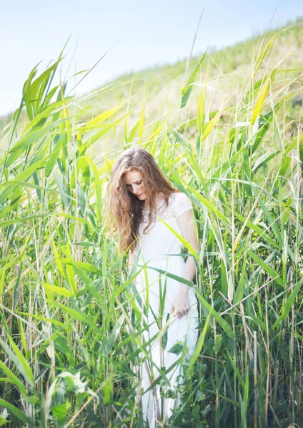 Etrafı sazlıklarla çevrili beyaz elbiseli genç bir kadın.