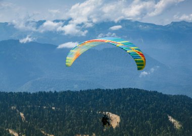 Sochi, Rusya, 26 Temmuz 2018: Yeşil dağ tarlaları yakınında uçan paraglider, doğa arka planı. Rosa Khutor bölgesinde dağlarda ekstrem sporlar