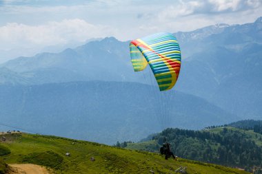 Sochi, Rusya, 26 Temmuz 2018: Yeşil dağ tarlaları yakınında uçan paraglider, doğa arka planı. Rosa Khutor bölgesinde dağlarda ekstrem sporlar