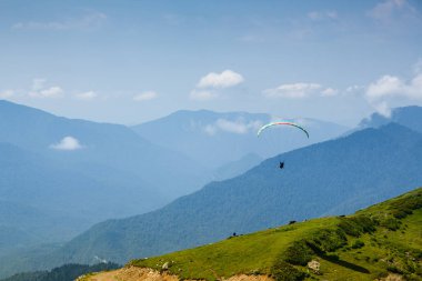 Sochi, Rusya, 26 Temmuz 2018: Yeşil dağ tarlaları yakınında uçan paraglider, doğa arka planı. Rosa Khutor bölgesinde dağlarda ekstrem sporlar
