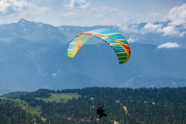 Sochi, Rusya, 26 Temmuz 2018: Yeşil dağ tarlaları yakınında uçan paraglider, doğa arka planı. Rosa Khutor bölgesinde dağlarda ekstrem sporlar