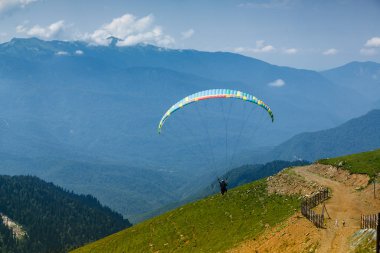 Sochi, Rusya, 26 Temmuz 2018: Yeşil dağ tarlaları yakınında uçan paraglider, doğa arka planı. Rosa Khutor bölgesinde dağlarda ekstrem sporlar