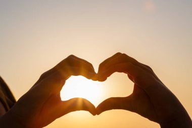 Gün batımının bulanık arka planında kalp yapan kadın eller