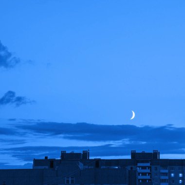 Gece gökyüzü ve yeni ay. Klasik mavi renkte. Altında bina var.