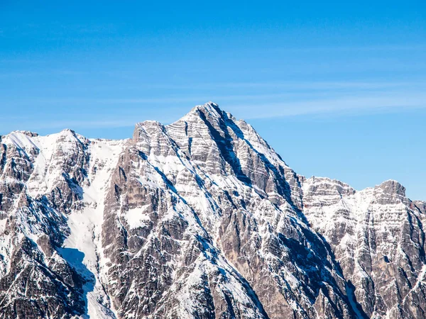 Vysoké skalnaté zasněžený vrchol na slunný zimní den s modrou oblohou. Alpský horský hřeben — Stock fotografie