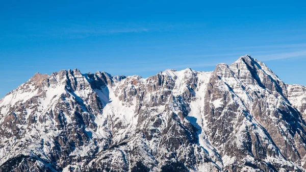 High rocky snowy peak on sunny winter day with blue sky. Alpine mountain ridge — Stock Photo, Image