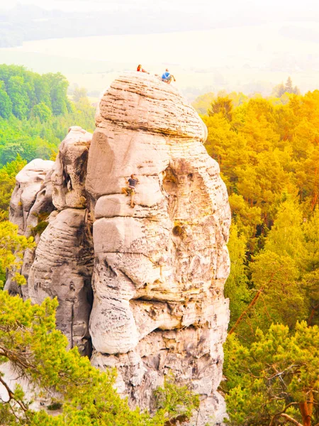 Bergsklättrare på sandsten torn. Man klättrar upp och två sitta på toppen. Bouldering i Bohemian Paradise, aka Cesky Raj, Tjeckien, Europa — Stockfoto