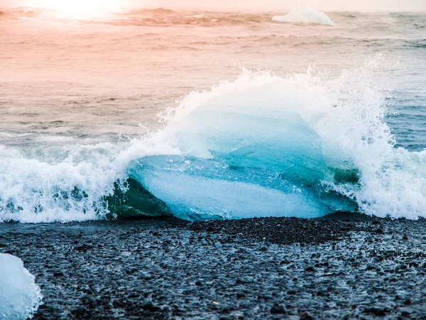 Buzdağları sphashed Jokulsarlon buzul Gölü, İzlanda yakınındaki gündoğumu zaman siyah sahilde dalgalar deniz tarafından — Stok fotoğraf