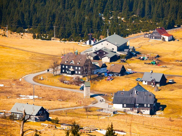 Bergsby Jizerka i Jizera Mountains i norra Böhmen, Tjeckien. Enkla hyddor runt mountain brook på solig vårdag med gult gräs och resten av snö fält — Stockfoto