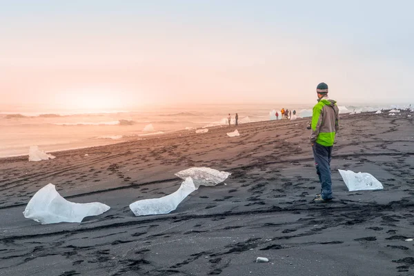 Bitar av is på svart sand, naturliga detaljer, Island. Man står på svarta stranden — Stockfoto