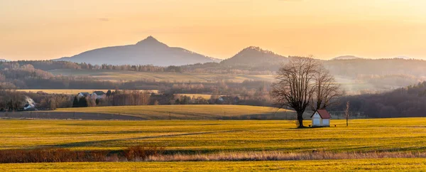 Paysage vallonné illuminé par le coucher du soleil du soir. Champs d'herbe verte et collines à l'horizontale. Campagne rurale printanière animée. Ralsko Mountain, République tchèque — Photo