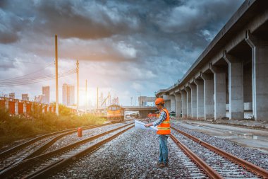 Kıdemli bir mühendis teftiş altında ve inşaat sürecini kontrol ediyor ve tren istasyonu platformunda çalışmalarını kontrol ediyor. İş yerinde güvenlik üniforması ve güvenlik kaskı takan mühendis.