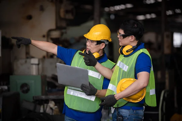 以笔记本电脑 穿着休闲服 头戴安全帽的工程师在工厂站对工厂工人的生产过程进行检查 — 图库照片
