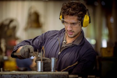 Güvenlik üniforması, cam ve kulaklık giyen endüstri işçisi fabrikada çalışan torna makinesini çalıştırıyor..