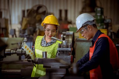Endüstri mühendisi ve işçi güvenlik üniforması giyiyorlar. Fabrika arka planında metal plaka makinesini kaydırıyorlar..