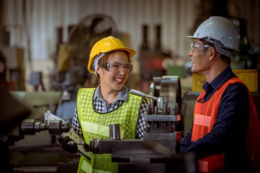 Endüstri mühendisi ve işçi güvenlik üniforması giyiyorlar. Fabrika arka planında metal plaka makinesini kaydırıyorlar..
