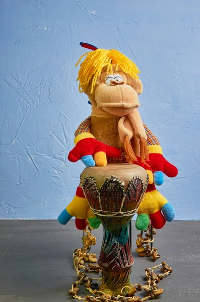 Brinquedo macaco com tranças e patas coloridas toca o tambor em um fundo azul — Fotografia de Stock