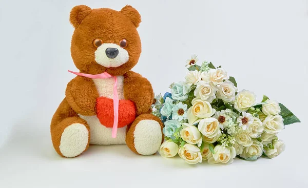 Urso de pelúcia com um coração vermelho em suas mãos e um buquê de flores em um fundo leve com lugar para texto . — Fotografia de Stock