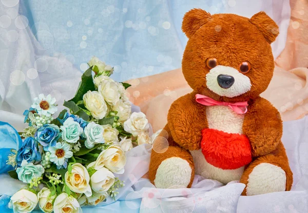 Urso de pelúcia com um coração vermelho nas mãos e um buquê de flores em um fundo festivo colorido com lugar para texto . — Fotografia de Stock