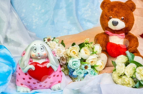 Um urso de pelúcia com um coração vermelho em suas mãos, e um coelho com um coração em suas mãos, um buquê de flores em um fundo de férias colorido com lugar para texto. Dia dos Namorados . — Fotografia de Stock