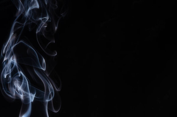 Abstract puffs of smoke on the left side of the frame on a dark background with a place for text, mysticism, fantasy.Copy space