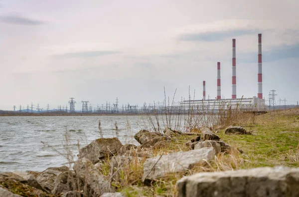 Cuatro tuberías de una central eléctrica en la orilla de un embalse en un día nublado de primavera, contra un cielo azul con nubes . — Foto de Stock