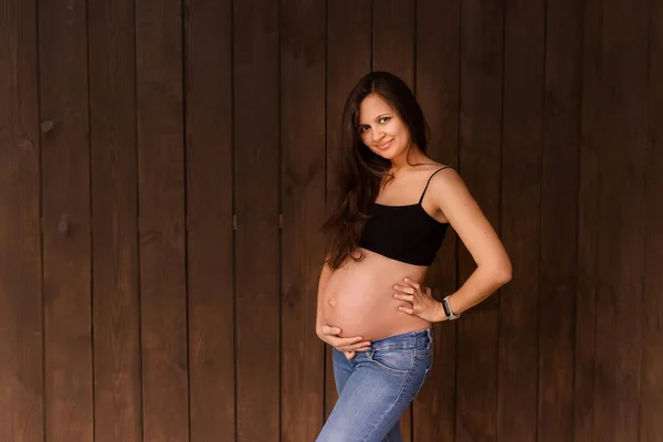 Pregnant Woman Jeans Black Top Holds Hands Belly Dark Brown — Stock Photo, Image