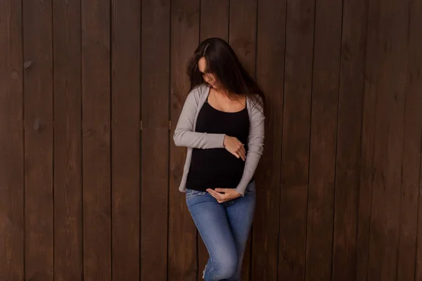 Kobieta Ciąży Dżinsach Czarny Top Trzyma Ręce Brzuchu Ciemnym Brązowym — Zdjęcie stockowe