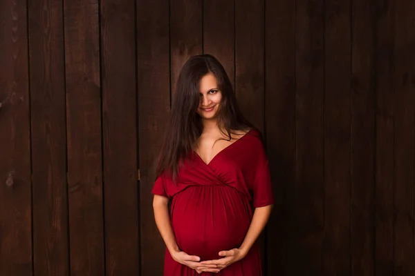 Pregnant Woman Red Dress Holds Hands Belly Dark Brown Background — Stock Photo, Image