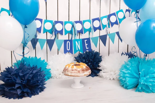 Photo zone with paper garlands, balloons, paper balls, pom poms, confetti and cream cake. Birthday cake. Smash cake. One year. Blue, dark blue, white colors