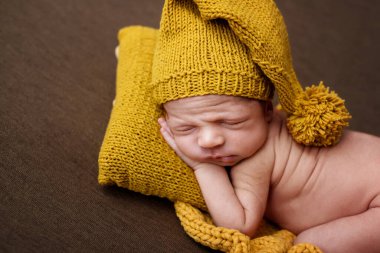 Kahverengi battaniyeli ve sarı yastıklı şirin yeni doğmuş bebek. Karanlık bir arka planda uyuyan bebek. Yeni doğan bebeğin yakın plan portresi. Bebek eşyaları paketleme şablonu. Çocuk odası. Tıbbi ve sağlıklı konsept.