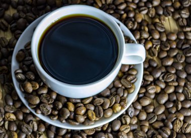 Kurabiyeli bir fincan kahve, kahve taneleri kahve bardağının yanındaki masaya saçılmış.