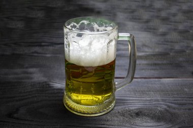 Koyu tahta arka planda bir bardak bira, köpüklü bira.