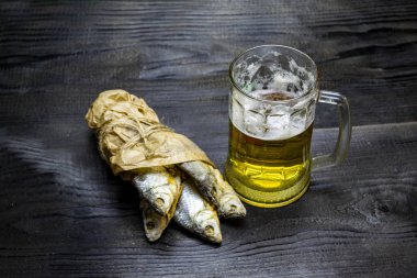 Koyu ahşap arka planda bir bardak bira, kağıt torbada kurutulmuş balık.