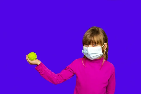 6歳から8歳の少女です医療用マスクにはウイルスのような緑色のボールがあります — ストック写真