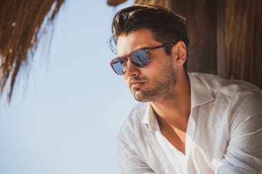 Güneş gözlüklü genç ve yakışıklı bir adam. Sıcak yaz ışıkları, beyaz bir gömlek giyiyor. Açık kısa sakal. Modaya uygun saç..