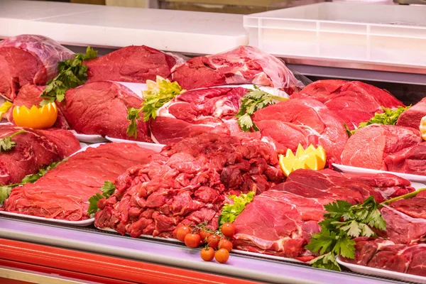 Bir alışveriş merkezinde kasaplık yapan et bölümü. Düzenli ve yaratıcı bir şekilde gösterilen çeşitli et türleri. Yiyecek süpermarketinin rafları. Süsleme ve süsleme için portakal ve sebze.
