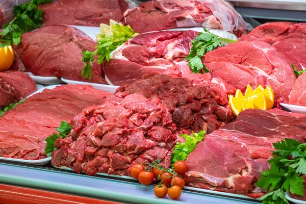 Bir alışveriş merkezinde kasaplık yapan et bölümü. Düzenli ve yaratıcı bir şekilde gösterilen çeşitli et türleri. Yiyecek süpermarketinin rafları. Süsleme ve süsleme için portakal ve sebze.